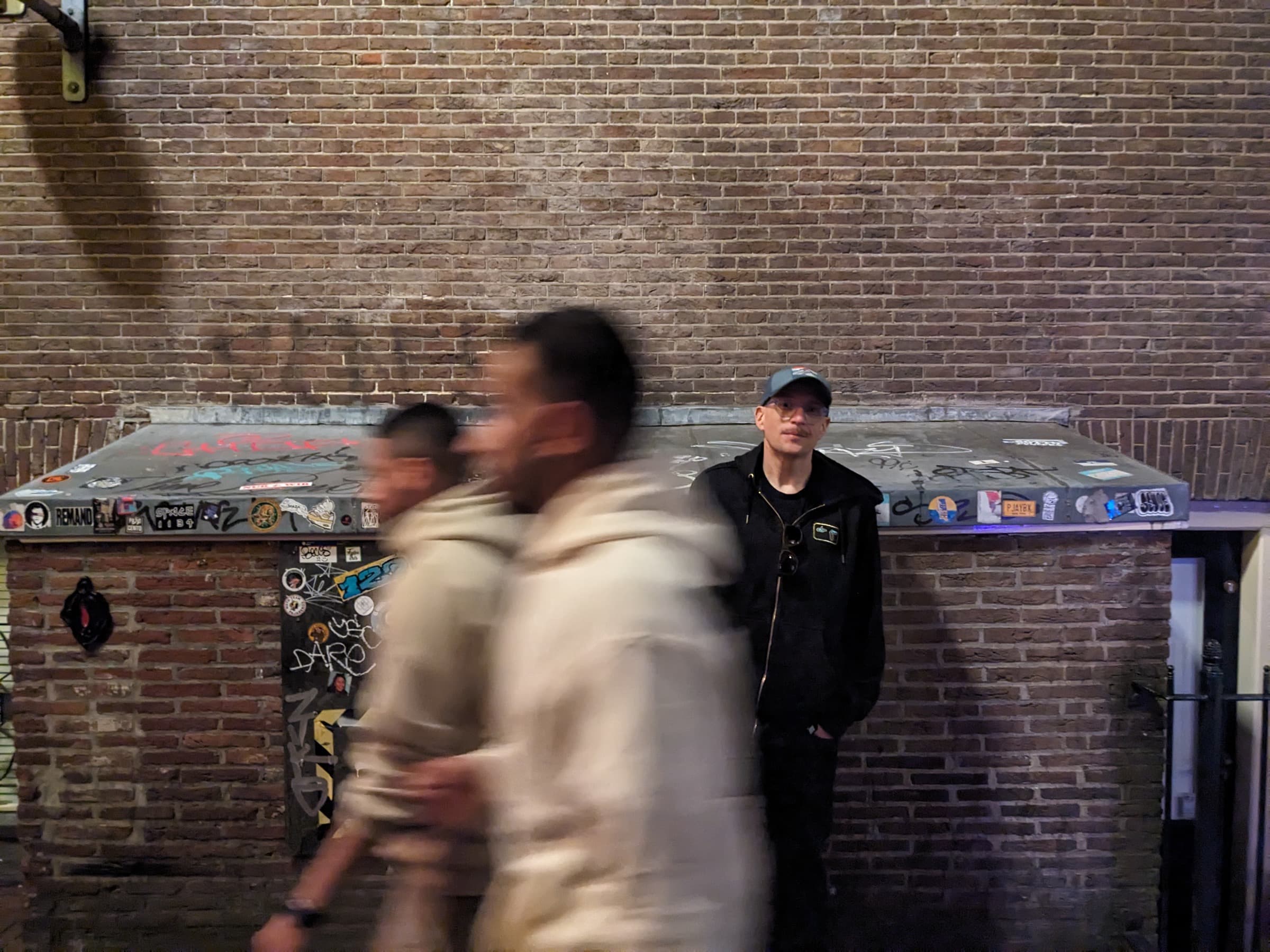 Justin standing by a dumpster on a brick-walled street at night